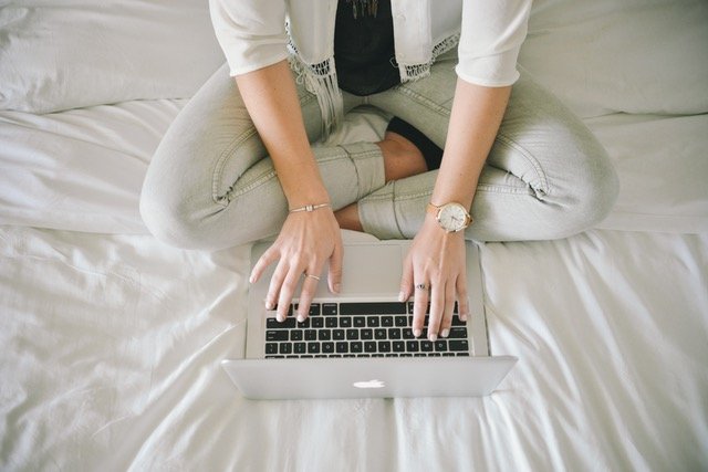 Woman on bed typing on laptop